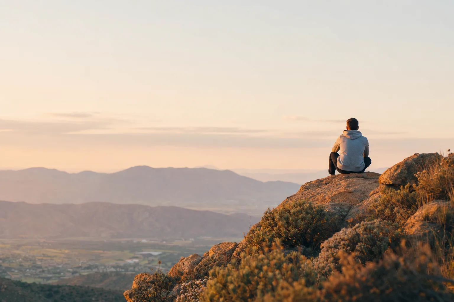 A person sitting on a hilltop at sunset looking out over the valley