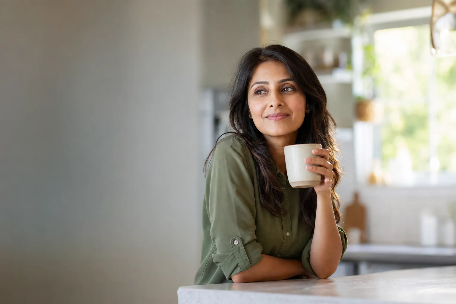 A woman leaning on a kitchen island with a mug of tea